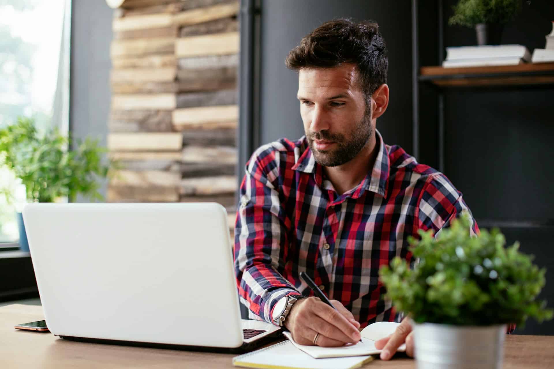 Person prüft Notizen neben einem Laptop am Arbeitsplatz