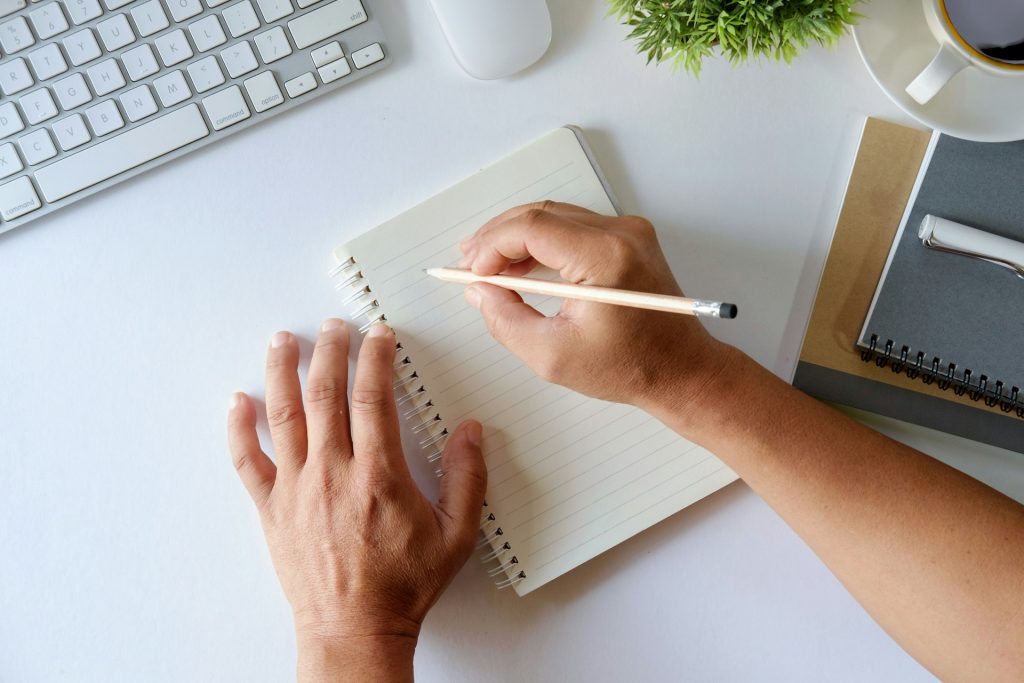 Man sieht einen Notizblock, der auf einem Schreibtisch liegt, Hände, die sich darüber beugen, sowie einen Stift, der zum Schreiben ansetzt. Das Bild soll das Notizen machen symbolisieren.
Ich führe ein papierloses Büro und liebe alles Digitale. Doch hin und wieder kann es sinnvoll sein, sich handschriftliche Notizen zu machen.