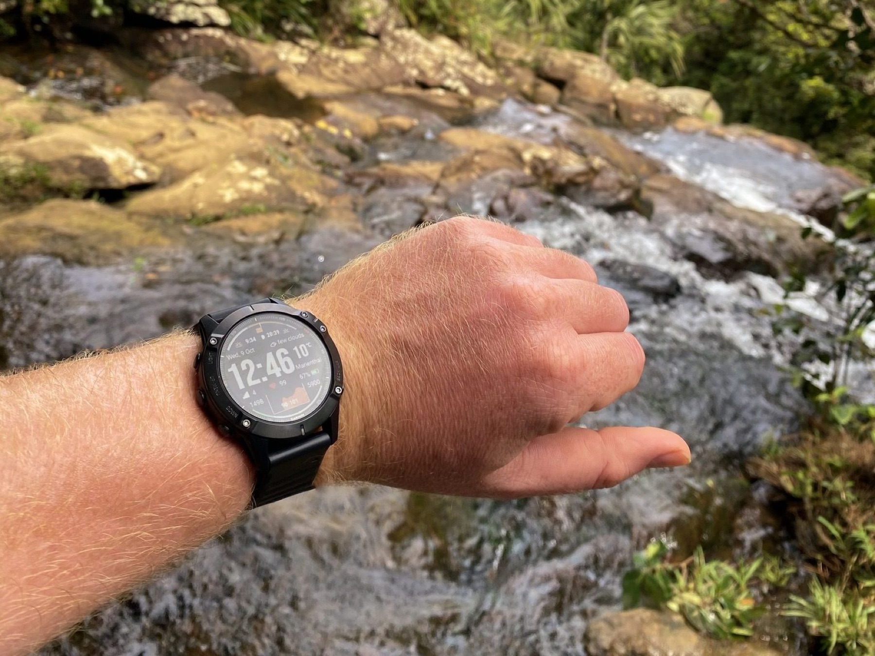 Sportuhr am Handgelenk vor einem Wasserfall im Freien